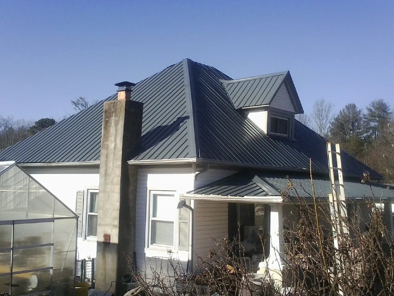 Dark blue standing seam metal roof on a white farmhouse with dormer — Slate & Tile Roof Repair by Roofing Brothers in Bringhurst