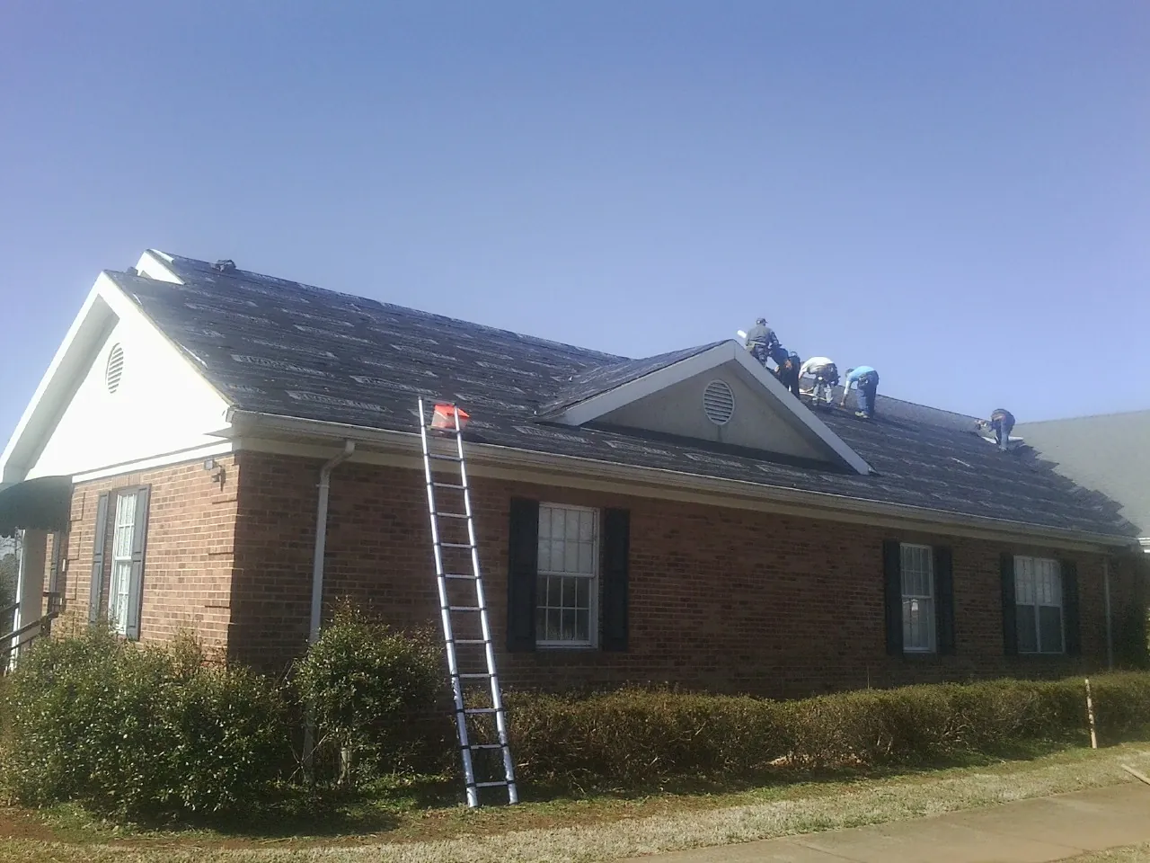 Crew tearing shingles off a brick ranch roof with a ladder set — Emergency Roof Repair work by our crew in Bringhurst