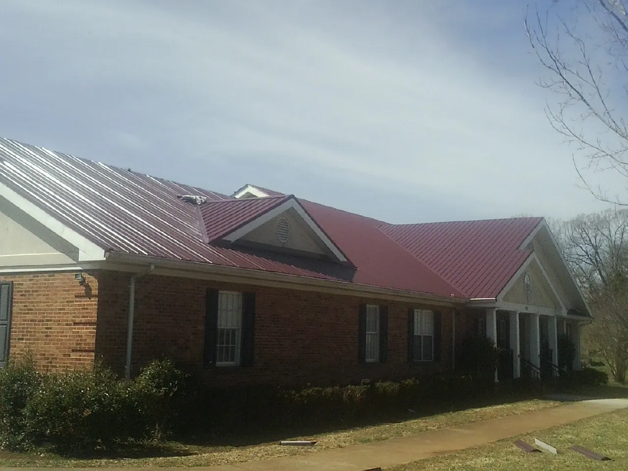 Red metal roof with gabled entries on a long brick building, from a Hail Damage Roof Repair job in Bringhurst