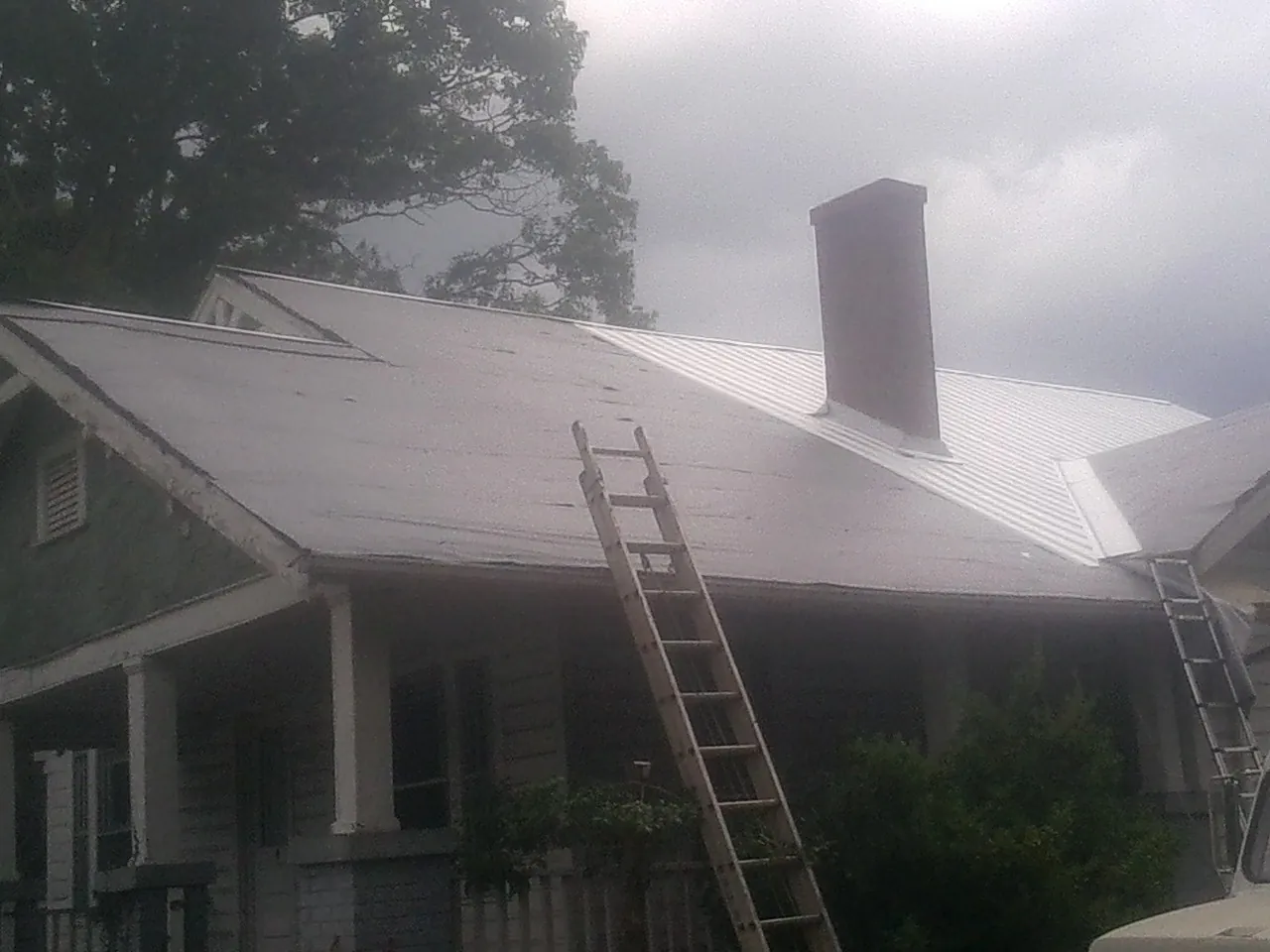 Ladders against a metal roof on an older home with a brick chimney in Bringhurst