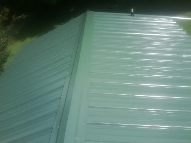 New green metal panels meeting at the ridge of a roof — Flat Roof Repair work by our crew in Bringhurst