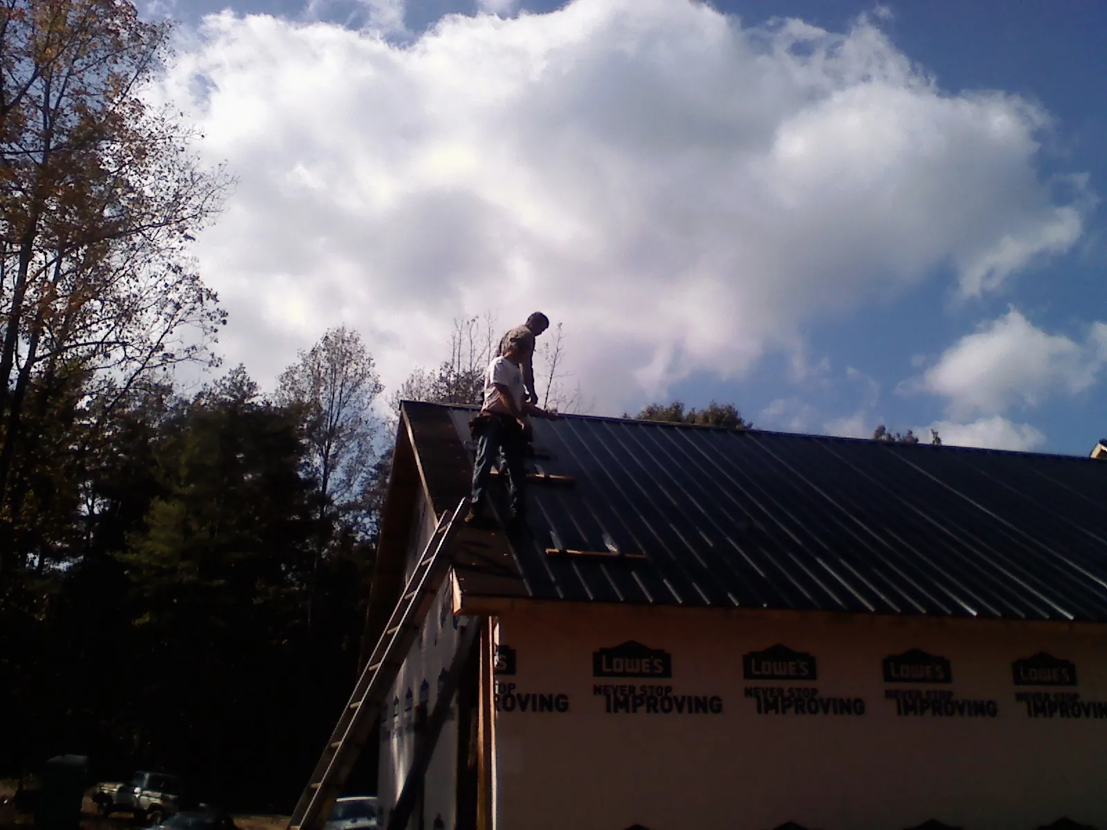 Roofer fastening dark metal panels high against a cloudy sky, from a Roof Inspection job in Bringhurst