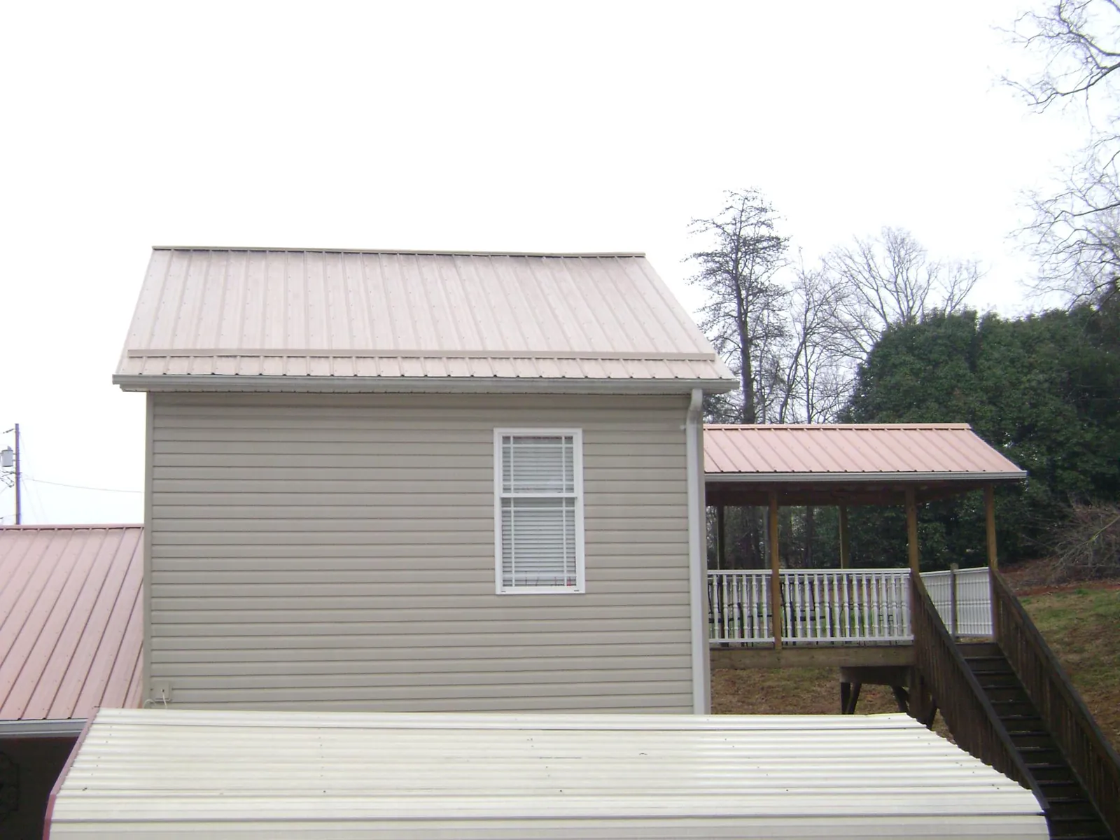 Tan metal roofs on a two story addition and attached porch, from a Roof Replacement job in Bringhurst